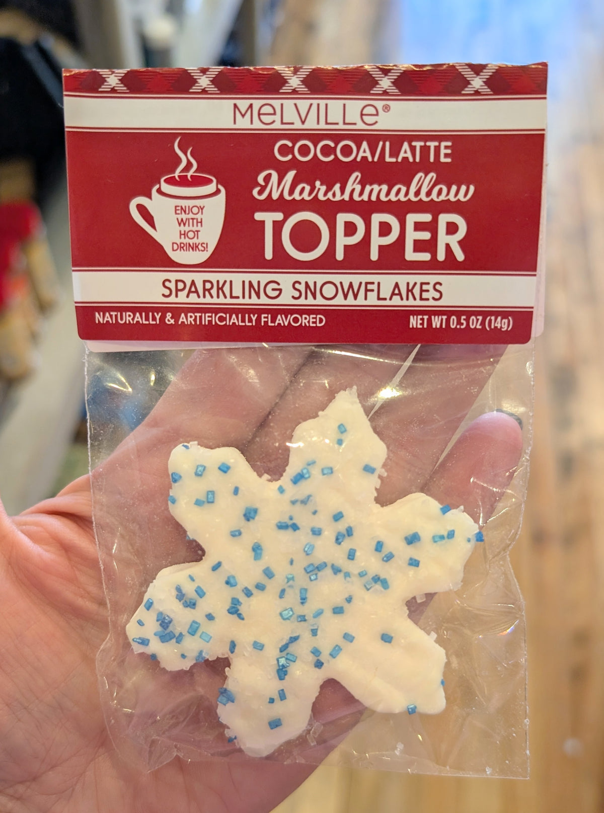 A snowflake shaped marshmallow topper in a package held by a hand with a wooden background