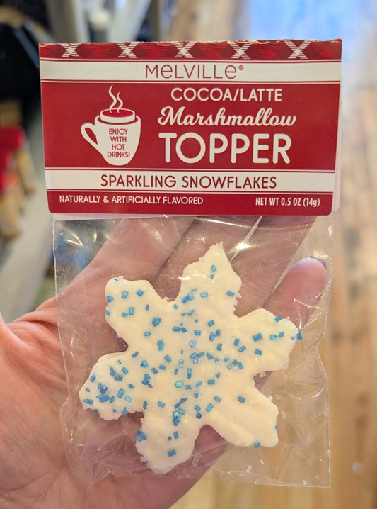 A snowflake shaped marshmallow topper in a package held by a hand with a wooden background